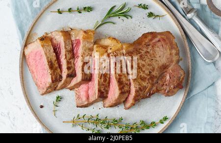 Keto ketogenic dieta bistecca di manzo, striploin su piatto grigio su sfondo bianco. Foto Stock