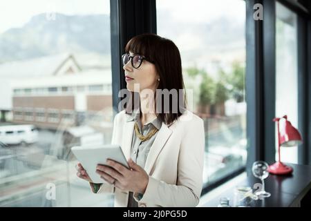 Prende sempre decisioni aziendali informate. Scatto di una giovane donna d'affari che usa un tablet digitale mentre si trova vicino a una finestra in un ufficio. Foto Stock