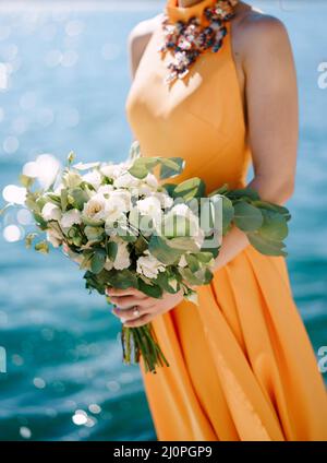 Donna in abito giallo con un bouquet di fiori si erge su uno sfondo di acqua. Primo piano Foto Stock