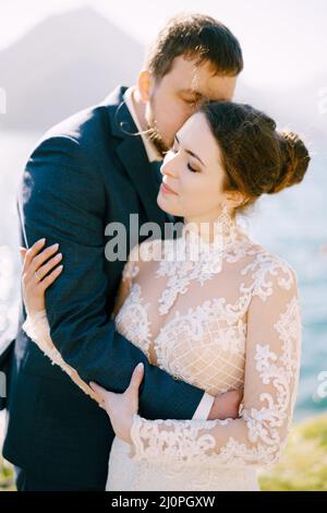 Lo sposo abbraccia la sposa e la bacia. Vista laterale. Primo piano Foto Stock
