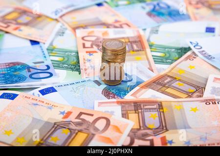 Una pila di monete in euro sullo sfondo di banconote in euro di diverse denominazioni Foto Stock