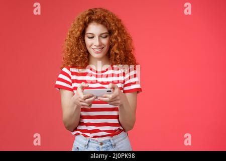 Redhead ragazza sciocco intorno coda d'attesa dentista giocare impressionante smartphone gioco tenere telefono orizzontale toccare cellulare schermo guardare t Foto Stock