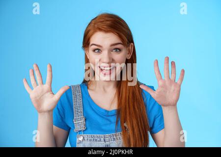 Close-up friendly joyful redhead caucasian girl, long ginger hairstyle, raise hands show number ten, counting dozer, explain fin Stock Photo