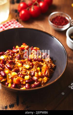 Chili con Carne con macinato di manzo, fagioli e mais in una ciotola scura su sfondo di legno. Cucina messicana e del Texas Foto Stock