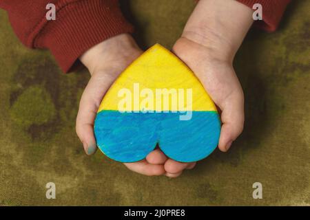 Le mani del bambino tengono un cuore dipinto nei colori della bandiera dell'Ucraina, primo piano, vista dall'alto Foto Stock