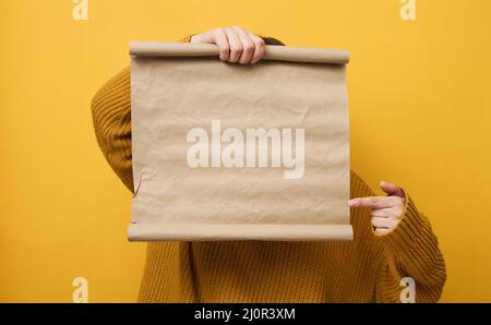 Donna in maglione arancione contiene rotolo di carta kraft marrone bianco. Luogo per un'iscrizione, pubblicità, informazioni Foto Stock