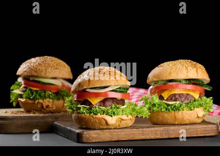 Cheeseburger con polpettine di manzo alla griglia, formaggio cheddar, pomodoro e lattuga su un asse di legno, sfondo nero Foto Stock