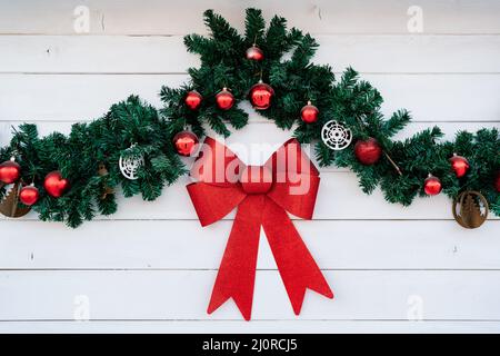 Decorazioni natalizie su sfondo bianco di legno - un ramo di abete con palline rosse e un grande arco rosso. Foto Stock