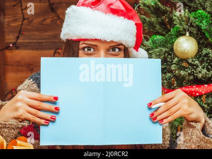 Modello caucasico femmina in un cappello Santa coperto la parte inferiore del suo viso con un foglio di carta bluastro, ha penna in mano. Let Foto Stock