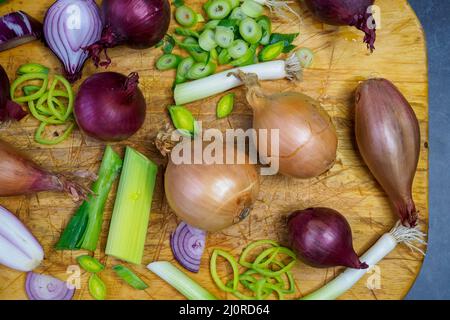 Diversi tipi di cipolla su tavola in legno. Cipolle, scalogni, cipolle rosse e primaverili. Foto Stock