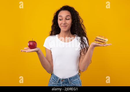 Ritratto di sorridente Lady Holding Apple e Burger Foto Stock