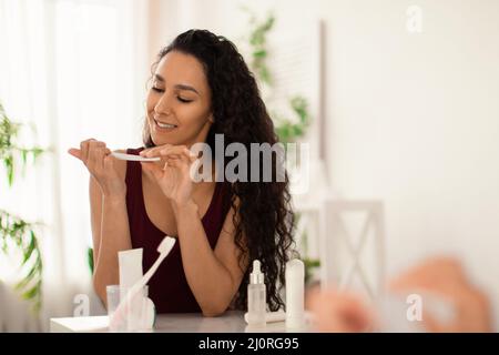 Bella donna millenaria bruna facendo le sue unghie di fronte allo specchio a casa, copia spazio Foto Stock