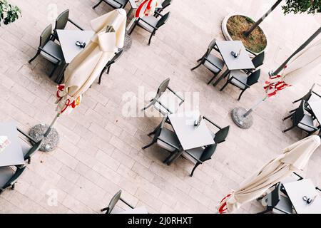 Vista dall'alto di tavoli e sedie vicino a ombrelloni ripiegati su piastrelle Foto Stock