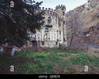 Antico castello abbandonato con balconi in rovina e finestre rotte nella zona boscosa delle montagne caucasiche in un giorno d'autunno Foto Stock