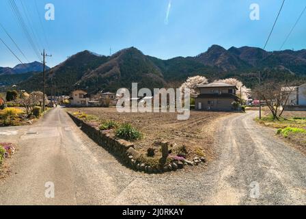 saitama, giappone - marzo 20 2022: Biforcazione stradale in una campagna giapponese della città di Chichibu con campi di raccolto e case di fava e le montagne di Bukō Foto Stock