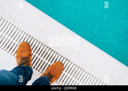 Piedi maschi in stivali marroni e jeans blu si levano in piedi al bordo della piscina. Primo piano Foto Stock