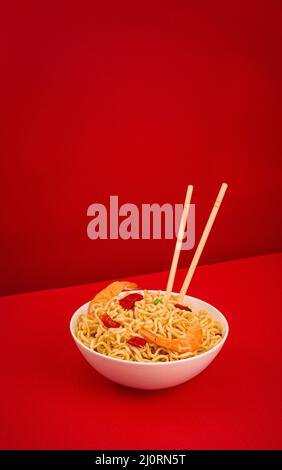 Tagliatelle asiatiche con gamberi in ciotola, fondo rosso minimo Foto Stock