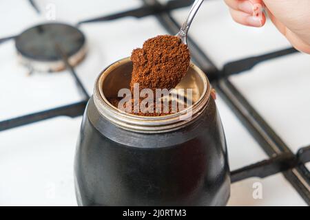 Il processo di versare caffè macinato fresco in una macchina per caffè geyser in piedi su una stufa a gas Foto Stock