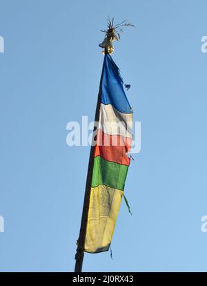 Colpo verticale di una bandiera di preghiera tibetana colorata su un bastone isolato su un cielo blu Foto Stock