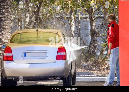 Un uomo non identificato sta pulendo la sua auto usando un'acqua ad alta pressione alla stazione di servizio Foto Stock