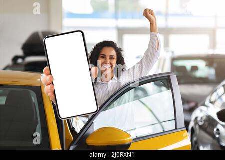 Donna bruna emozionale che sceglie la nuova auto, mostrando il telefono cellulare Foto Stock