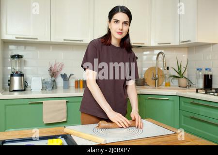 Giovane bella bruna caucasica donna 25s cottura in cucina, guardare la macchina fotografica e sorridente. Foto Stock
