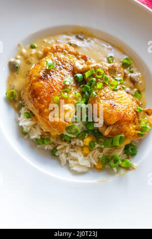 Cosce di pollo disossate e saltate su un letto di riso con piselli e mais serviti con un ricco fungo, vino bianco e salsa di panna. Cucina casalinga di famiglia Foto Stock