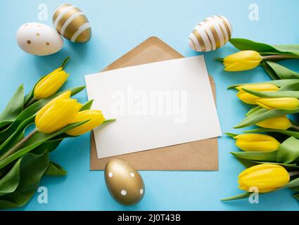 Auguri di Pasqua: Tulipani gialli, uova dorate e bianche su sfondo blu. Una lettera con spazio per la copia. Vacanze di primavera. Foto Stock