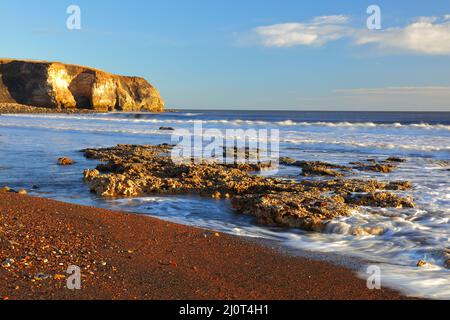 Luce del mattino a Blast Beach con rocce calcaree di magnesio nel primo piano, Seaham, County Durham, Inghilterra, Regno Unito. Foto Stock