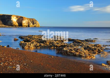 Luce del mattino a Blast Beach con rocce calcaree di magnesio nel primo piano, Seaham, County Durham, Inghilterra, Regno Unito. Foto Stock