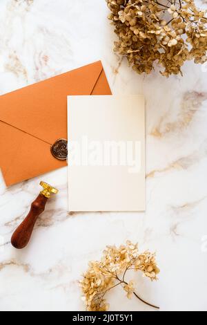 Design di carte di invito per matrimoni di lusso. Carta bianca, busta di bronzo, fiori secchi su tavolo da scrivania in marmo vista dall'alto. Foto Stock