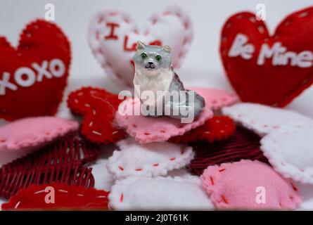 Una statuetta di gatto si siede su un mucchio di cuori fatti a mano di San Valentino. Foto Stock