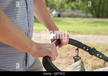 Un giovane papà che cammina nel parco con un bambino in un passeggino. Primo piano delle mani degli uomini con un passeggino. Concetto di Father's Day. Foto di alta qualità Foto Stock