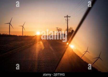 Turbine eoliche e pali telefonici lungo una strada rurale nel Midwest americano al tramonto Foto Stock