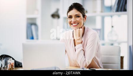 Tutto sta andando secondo il programma oggi. Ritratto di una giovane e attraente donna d'affari che lavora su un laptop nel suo ufficio. Foto Stock