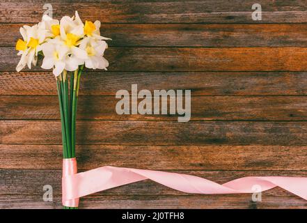 Bouquet di naffodils con nastro rosa su sfondo di grunge retrò in legno con spazio di copia. Mock up per il testo, per le frasi, per lett Foto Stock