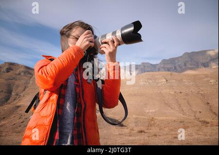 Donna caucasica fotografo paesaggio con grande obiettivo e fotocamera professionale scatta foto in montagna sullo sfondo di e. Foto Stock