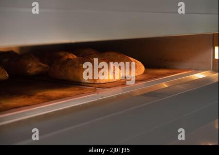 In un forno industriale vengono cotti tre pani di pane. Produzione artigianale di pane Foto Stock