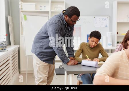 Ritratto della vista laterale dell'insegnante afro-americano che aiuta la giovane ragazza durante la lezione in aula scolastica, spazio di copia Foto Stock