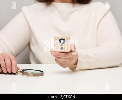 Mano femmina che tiene un cubo di legno con un punto interrogativo, concetto di risposte e domande, suspense e metodi di soluzione Foto Stock