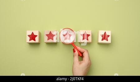 Cinque stelle rosse e una mano con lente di ingrandimento in plastica su sfondo verde. Valutazione della qualità dei servizi e dei beni, alta Foto Stock