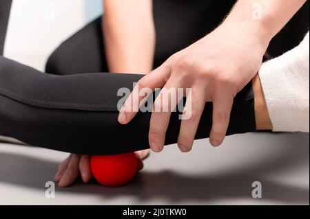 Physiotherapist teaches self-massage with red balls, patient with leg injury. Treatment of sports injuries. Practical use. Rehab Stock Photo