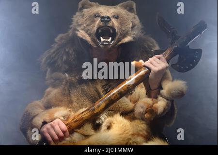 Ritratto di un uomo scandinavo sciamano con ascia sulle mani e pelle di orso sulla testa. Uomo caucasico vestito di sci animale Foto Stock