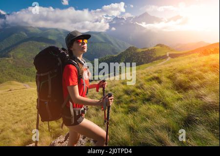 Una ragazza turistica con uno zaino ammira il tramonto dalla montagna. Il viaggiatore sullo sfondo di montagne e nuvole a s. Foto Stock