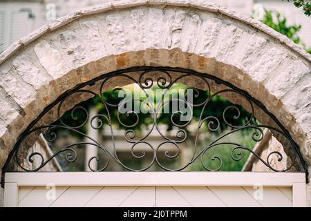 Traliccio in metallo forgiato ad arco in una recinzione in pietra. Primo piano Foto Stock