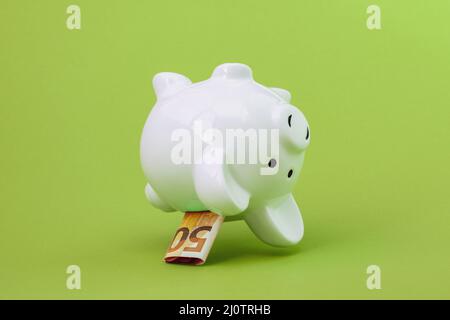 Piggy banca con cinquanta Euro caduta sullo sfondo verde Foto Stock