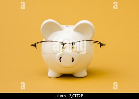Primo piano di una banca piggy indossando occhiali sullo sfondo giallo Foto Stock