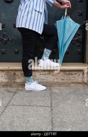 Donna irriconoscibile appoggiata sul suo ombrello blu in una porta Foto Stock