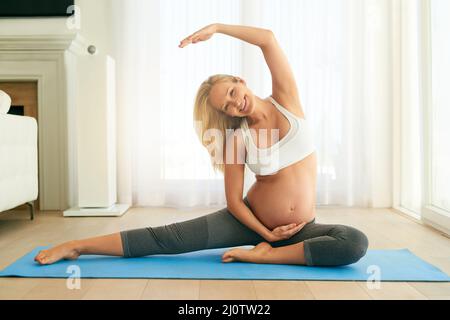 Yoga per due. Shot di una donna incinta che fa yoga su un materassino di esercitazione a casa. Foto Stock