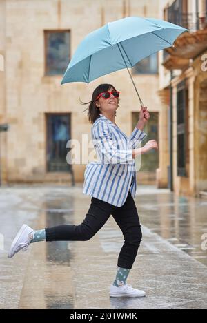 Donna che salta sopra una pozzanghera in una giornata piovosa Foto Stock